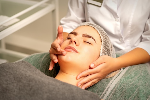 Masaje facial Hermosa mujer blanca caucásica con un masaje facial con los ojos cerrados en un salón de spa