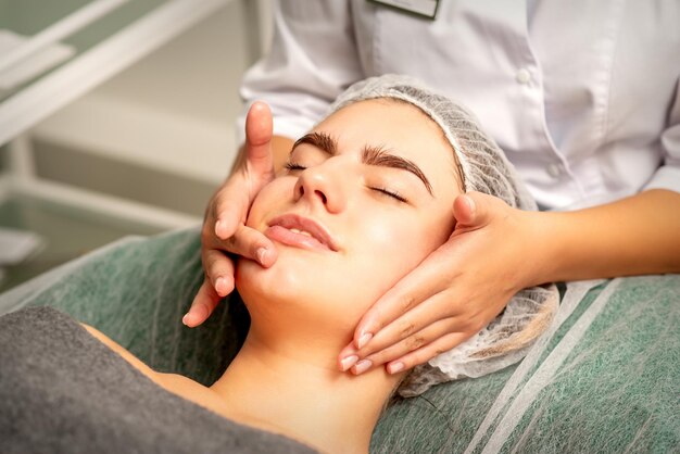 Masaje facial Hermosa mujer blanca caucásica con un masaje facial con los ojos cerrados en un salón de spa