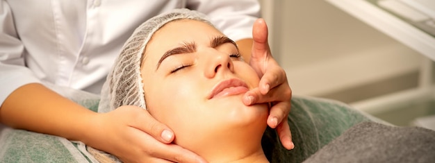 Masaje facial Hermosa mujer blanca caucásica con un masaje facial con los ojos cerrados en un salón de spa