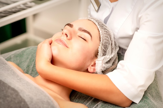 Masaje facial Manos de un masajista masajeando el cuello de una joven mujer caucásica en un salón de spa el concepto de masaje de salud