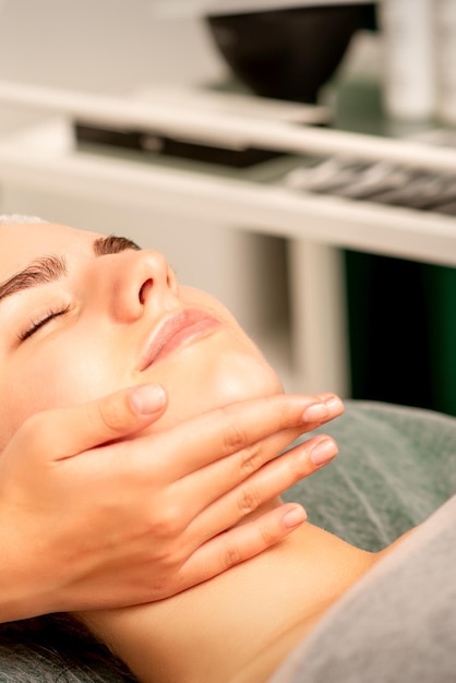 Masaje facial Manos de un masajista masajeando el cuello de una joven mujer caucásica en un salón de spa el concepto de masaje de salud