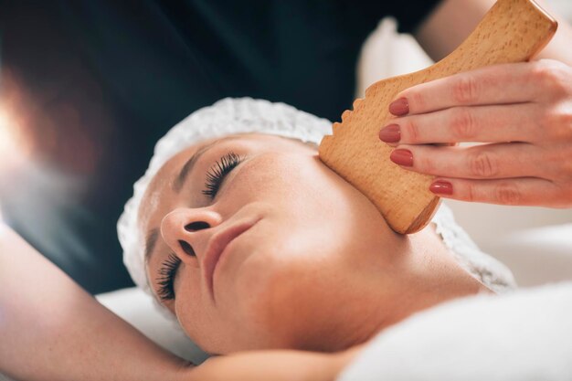 Masaje facial con masajeador de forma de placa Gua Sha de madera