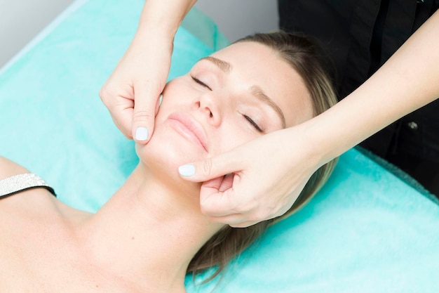 Masaje facial Primer plano de una mujer joven que recibe un masaje de spa en un salón de belleza spa Cuidado de la belleza facial Cosmetología Fondo turquesa