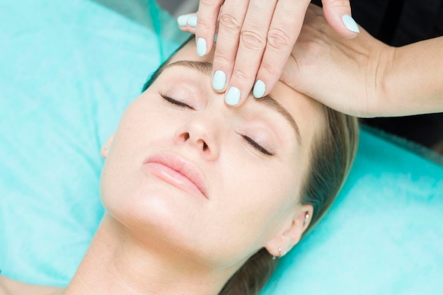 Masaje facial Primer plano de una mujer joven que recibe un masaje de spa en un salón de belleza spa Cuidado de la belleza facial Cosmetología Fondo turquesa