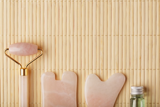 Masaje gua sha hecho de rodillo de cuarzo rosa natural, piedra de jade y aceite, sobre un fondo de bambú para el cuidado de la cara y el cuerpo.