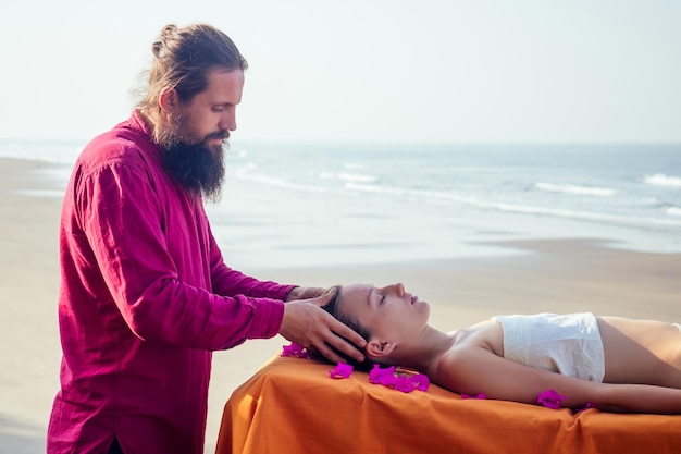 Masaje terapéutico a la orilla del mar tropical. Mujer de masaje relajante ayurvédico en el salón de spa recibiendo masajes en la playa de vacaciones. niña acostada en el procedimiento de tratamiento de mesa