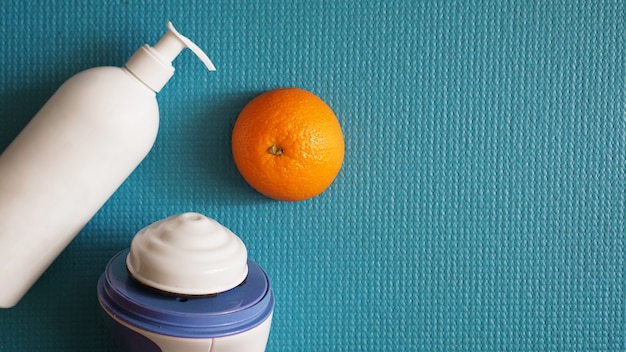 Masajeador eléctrico para celulitis. Masajeador loción, naranja y masajeador anticelulítico sobre fondo azul.