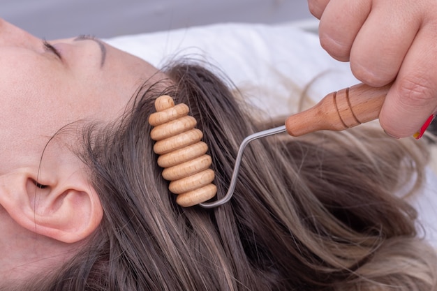 Masajee las raíces del cabello de la niña con el masajeador de rodillos de madera, primer plano. Masajee las raíces del cabello para que el cabello crezca sano y exuberante. Hermoso cabello fuerte y bien cuidado