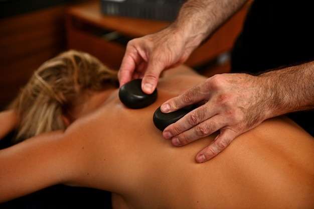 Masajista colocando piedras calientes terapéuticas en la espalda de la mujer. Masaje ayurvédico con piedras calientes en el moderno salón de spa. Concepto de cuidado del cuerpo