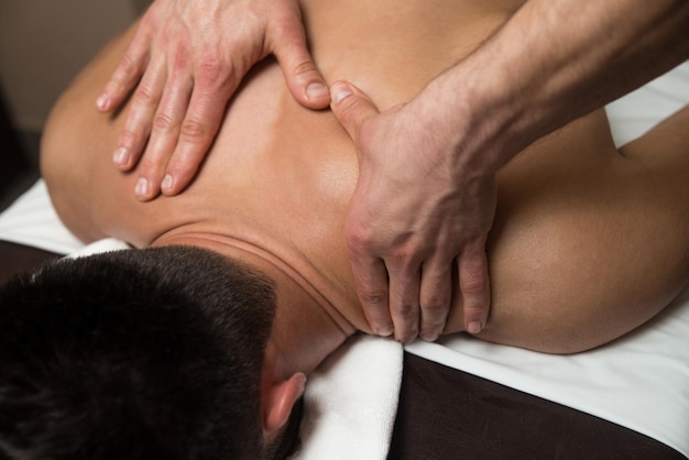 Masajista haciendo masaje en el cuerpo del hombre en el salón de spa