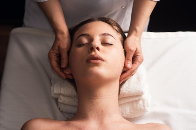 Masajista haciendo masaje facial a mujer joven en mesa de masaje Concepto de tratamientos de spa de masaje Primer plano