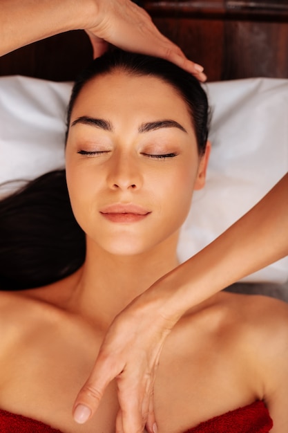 Foto masajista profesional. atractiva mujer morena descansando con los ojos cerrados durante el procedimiento en el salón de belleza