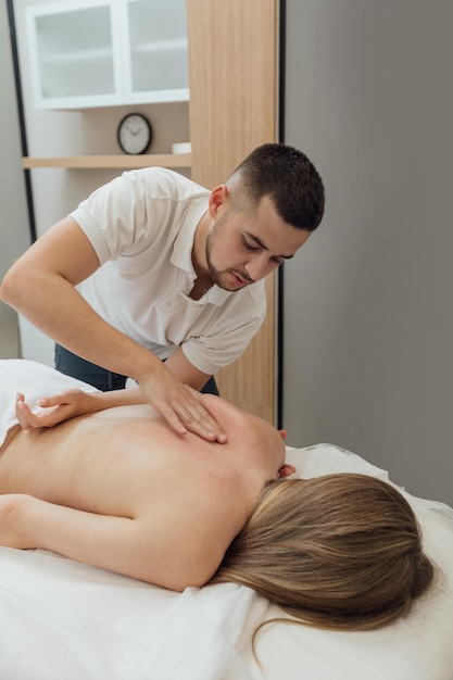 El masajista profesional hace un masaje corporal reparador en el cuerpo de una mujer acostado boca abajo en la mesa de masaje en el salón de spa