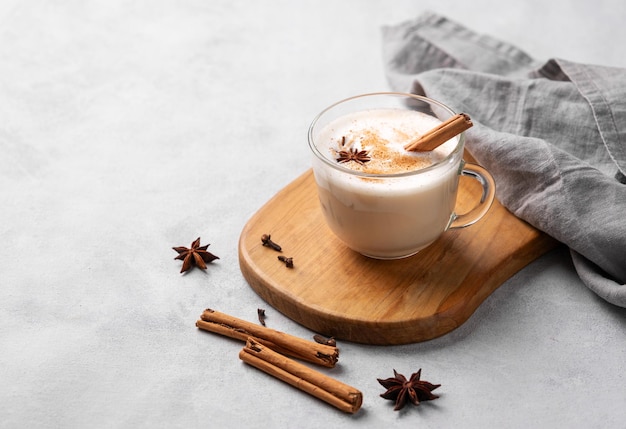 Masala chai latte indiano tradicional em um copo de vidro Bebida quente com especiarias de leite e ervas em uma tábua de madeira em um fundo claro