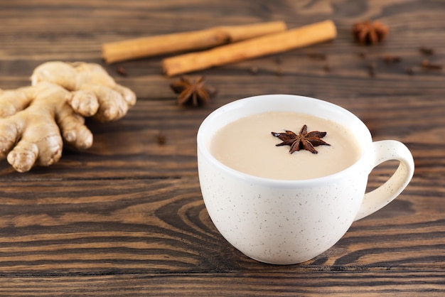 Masala Chai mit Kokosmilch-Anis-Zimt-Ingwer-Pfeffer in einer Tasse auf einem Holztisch