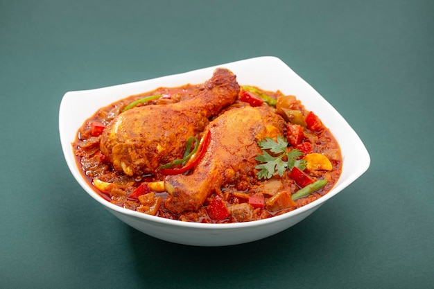 Masala de frango indiano, molho espesso de frango picante indiano guarnecido com folha de coentro, pimenta vermelha e verde que é organizada em uma tigela de cerâmica branca sobre fundo verde, isolado.