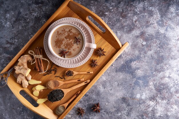 Masala-Tee in einer Tasse mit Gewürzen Ingwer, Zimt, Anis, schwarzem Pfeffer auf grauem Sone-Tisch