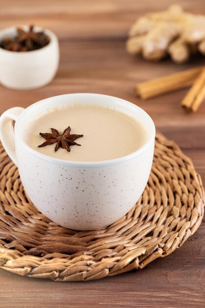 Masala-Tee mit Milchanis und Gewürzen in einem Becher auf einem Holztisch