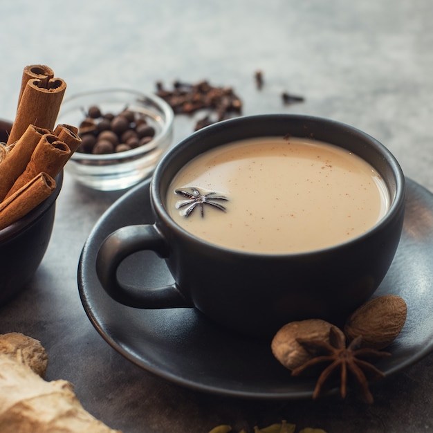 Masala-Tee. Traditioneller indischer Chai in schwarzer Tasse mit Gewürzen auf grauem Hintergrund.