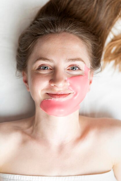 Máscara algínica en la cara de una mujer joven en un procedimiento cosmético de salón de belleza para hacer que la piel sea más joven y fresca sobre fondo blanco