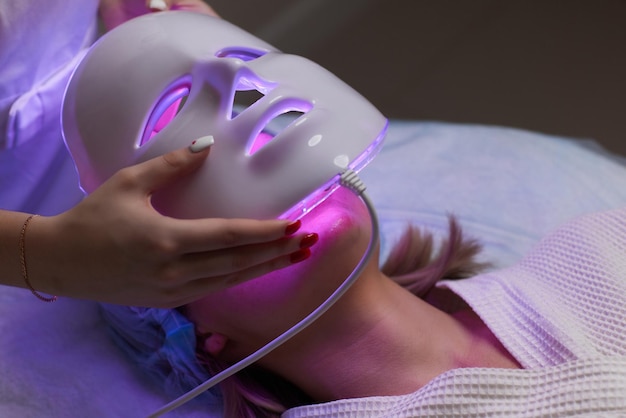 Máscara antienvelhecimento de luz led para cuidados com a pele facial em um spa em câmera lenta uma mulher deitada em um sofá em uma especificação