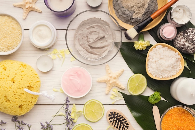 Máscara de barro de cosmetología y producto de spa natural sobre fondo blanco de madera con hojas verdes. Concepto de cuidado de la piel, vista superior