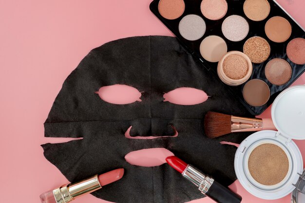 Máscara cosmética negra y maquillaje en fondo rosa con espacio de copia