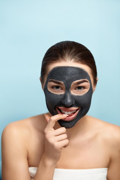 Máscara de cuidado de la piel facial de mujer de belleza Retrato de una mujer hermosa con una máscara negra de arcilla en la cara
