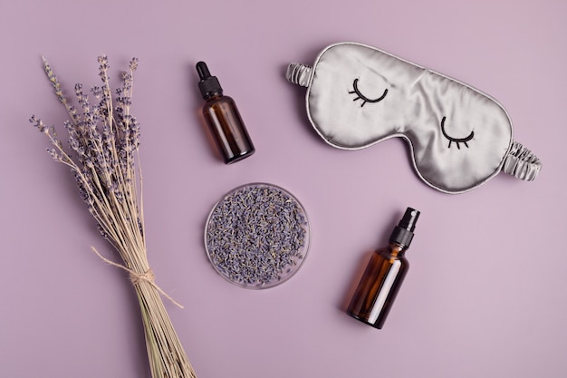 Máscara de dormir e óleo essencial de lavanda sobre fundo roxo. tratamento natural da insónia, relaxamento, anti-stress, conceito de qualidade do sono. camada plana, vista superior