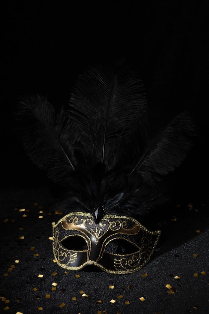 Foto máscara de ouro de carnaval com penas e confetes em fundo preto