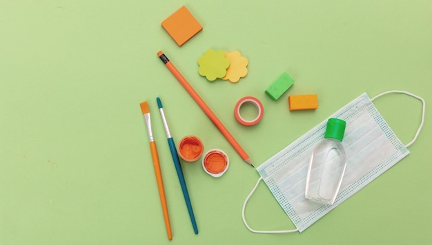 Foto máscara de proteção médica, gel de desinfetante de mãos e suprimentos escolares em fundo verde pastel, vista superior de volta aos dias de coronavírus na escola