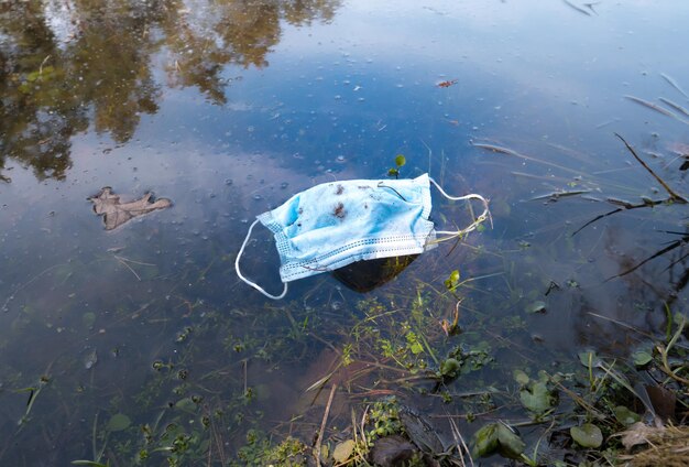 Máscara de proteção médica na água do lago da cidade Consequência do coronavírus COVID19 Conceito de lixo médico de poluição ecológica Lixo e lixo no parque