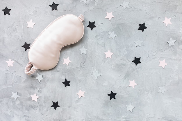 Máscara de sleepink de olho de cetim rosa e confete de estrelas de papel rosa e dourado sobre fundo cinza