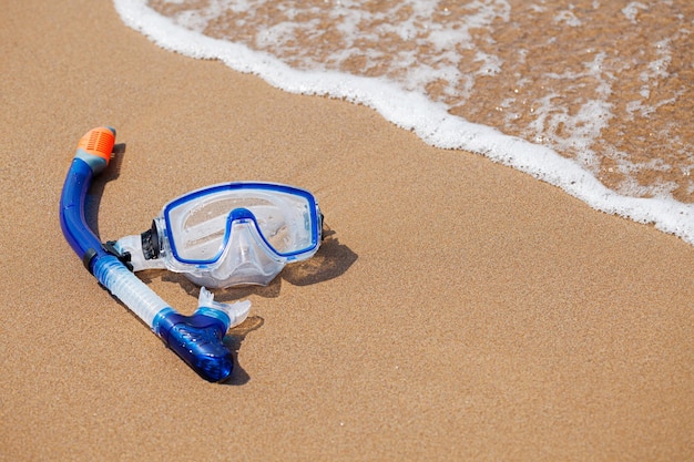Máscara e snorkel nas ondas no foco seletivo da praia arenosa
