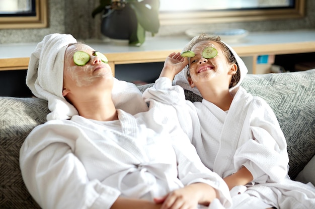 Máscara facial de cuidados com a pele fresca e tratamento de pele saudável para unir mãe e filha dia de spa em casa diversão sorridente e brincalhona criança e pai relaxando com pepino sobre os olhos na rotina de higiene