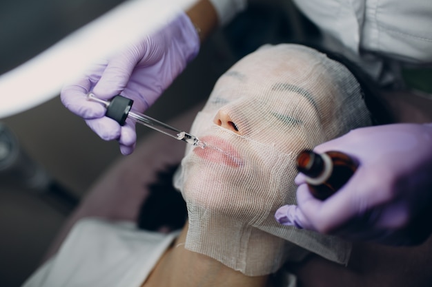 Máscara facial de parafina com atadura de gaze terapia jovem mulher recebendo tratamento de pele facial. Esteticista Pouring Wax Aplicação e hidratação dos lábios.