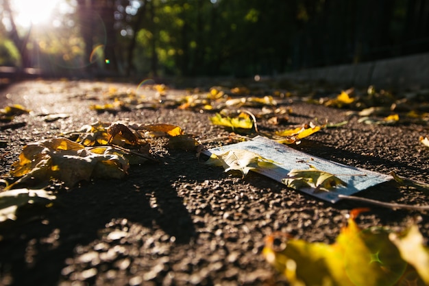 Máscara facial médica deitada no asfalto com folhas de outono ao ar livre