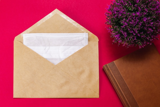 Foto máscara facial médica em um envelope vermelho com um bloco de notas marrom e uma flor lilás