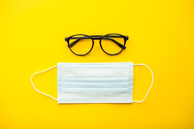 Foto máscara y gafas protectoras médicas laicas planas sobre fondo amarillo brillante