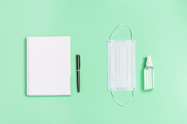 Máscara médica de rosto, desinfetante para as mãos, caderno, caneta.