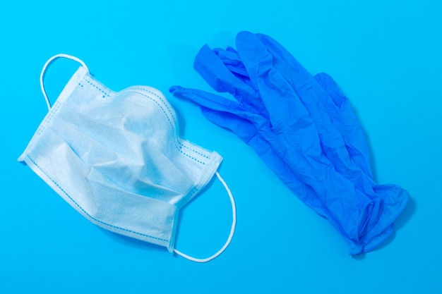 Máscara médica y guantes sobre un fondo azul.