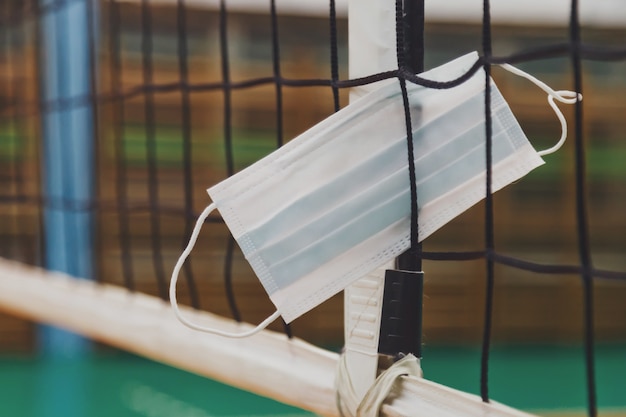 Máscara médica na rede de vôlei em um antigo pavilhão desportivo vazio com torre de árbitro. plano de fundo para o jogo de vôlei de equipe. conceito de obter esporte, estilo de vida e sucesso durante o período de pandemia. copie o espaço