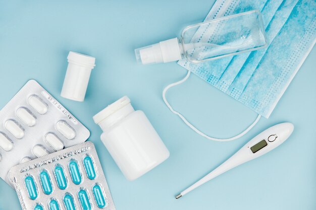 Máscara médica, pílulas e termômetro sobre fundo azul.