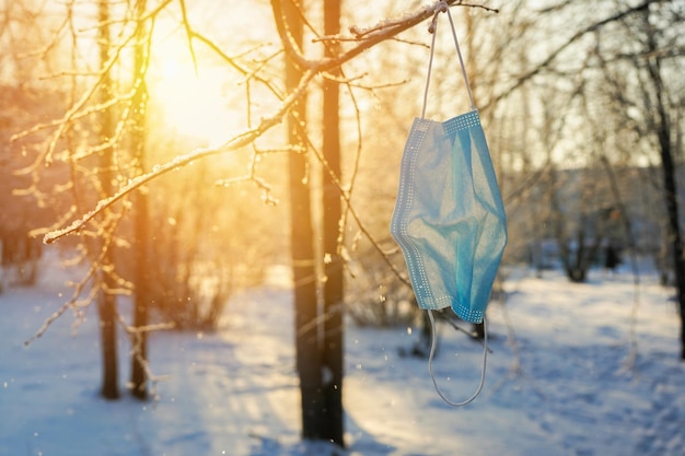 Máscara médica usada colgando de la rama de un árbol, invierno