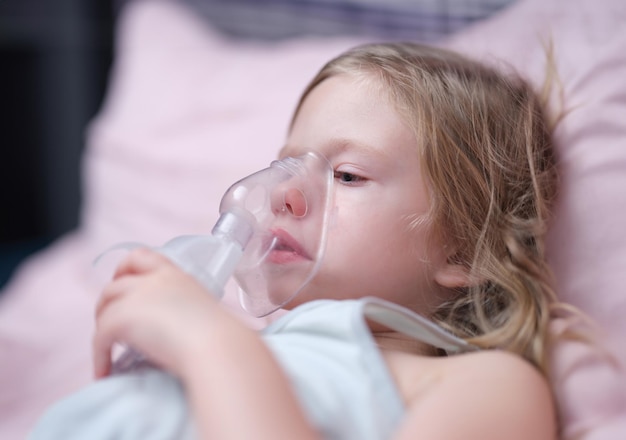 Máscara de oxígeno de una niña linda en la cara en la cama en el hospital neumonía asma y concepto de nebulizador