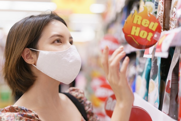 Máscara protetora da mulher asiática no suppermarket durante a epidemia covid-19.