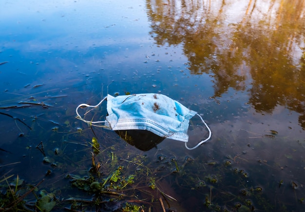 Foto máscara protetora médica na água do lago da cidade. consequência do coronavírus (covid-19). poluição de ecologia, conceito de lixo médico. lixo e lixo no parque.