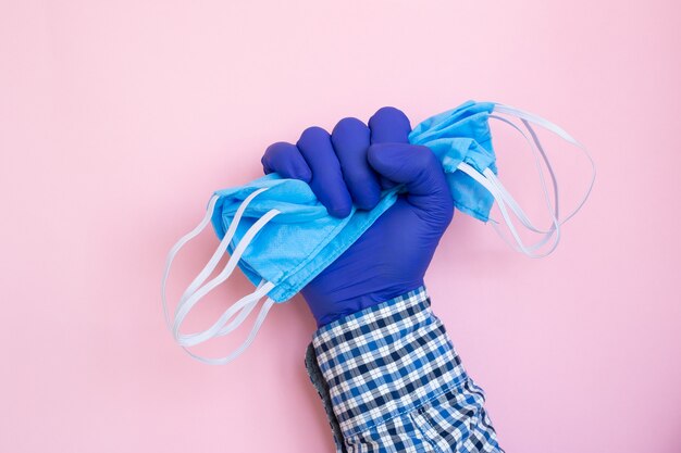 Foto máscara protetora ou máscara médica na mão protegida por luvas azuis em fundo rosa. doença do coronavírus. conceito de saúde e medicina, prevenção de vírus.