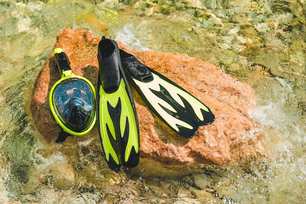 Foto máscara de snorkel con aletas en roca en agua de mar.