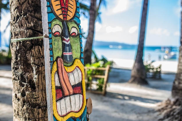 Máscara tiki en una palmera con la playa al fondo